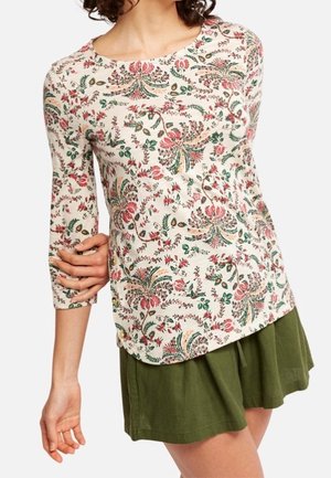 Femme portant un haut beige à manches longues avec un motif floral et un short ample vert olive.