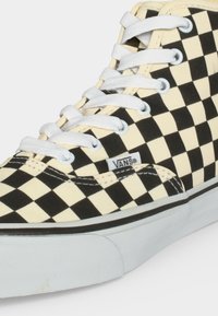 Δερμάτινο sneaker Vans με ασπρόμαυρο καρό μοτίβο, λευκά κορδόνια και λευκή λαστιχένια σόλα με ετικέτα Vans στο πλάι.