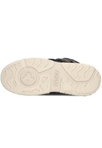 Semelle de sneaker noire avec un motif de traction en caoutchouc blanc texturé, présentant un logo circulaire au centre et un onglet surélevé le long du bord.