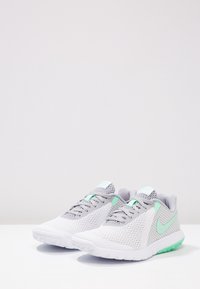 Zapatillas Nike con parte superior de malla blanca transpirable, acentos grises y logo verde menta. Suela ligera con patrón texturizado para tracción.
