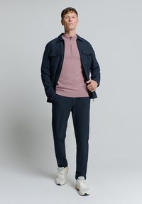 Navy jas met voorzakken, roze lang-oevers ritshemd, donkere broek en witte sneakers. Gladde stof, op maat gemaakte pasvorm.