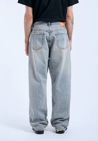 Vaqueros de denim azul claro con un ajuste relajado, que cuentan con dos bolsillos traseros y una etiqueta naranja de marca en la cinturilla.