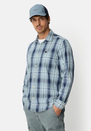 Lichtblauw geruit overhemd met knoopsluiting en een borstzak, gedragen met een blauwe pet en gecombineerd met grijze cargoshorts.