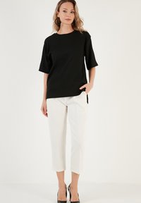 Black textured top with short, slightly flared sleeves, paired with white cropped trousers and black heeled shoes. Simple, modern design.