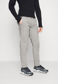 Chino grigi in cotone con tasche laterali e vestibilità slim, abbinati a sneakers nere e grigie con dettagli in rete e gomma.