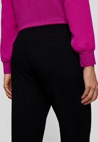 Black tailored pants with a smooth texture and a back pocket detail, paired with a vibrant pink long-sleeve blouse featuring elasticated cuffs.