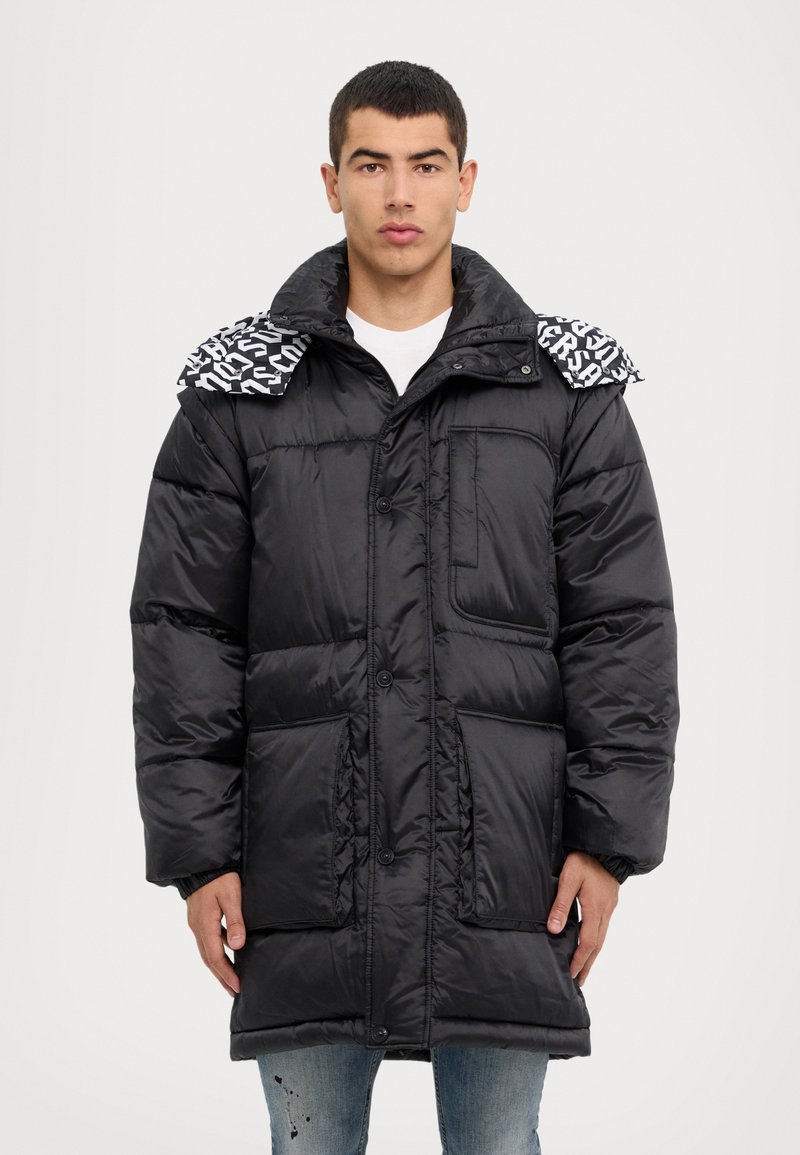 Chaqueta de plumas negra con cierre de botones, bolsillos frontales y un cuello de patrón en blanco y negro en contraste. Textura suave y brillante.