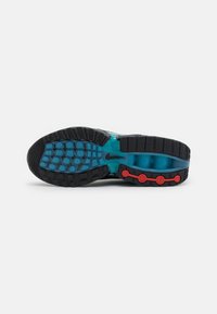 Semelle en caoutchouc noire et bleue d'une chaussure de sport avec des accents circulaires rouges et des motifs de crampons sur fond blanc.