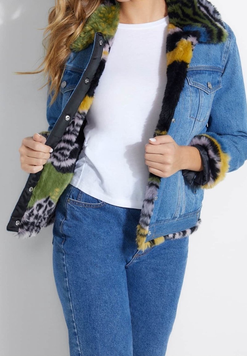 Chaqueta de mezclilla con un forro de piel sintética multicolor. Presenta patrones en verde, amarillo, negro y gris. Cierres de botón en el frontal y detalles en las mangas.