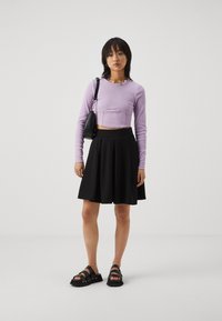 Purple ribbed long-sleeve crop top, black pleated skirt, and black multi-strap sandals. Simple design, fitted shape, and textured fabric.