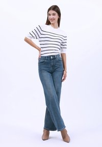 Suéter blanco de manga corta con rayas negras, combinado con jeans azules de cintura alta. El atuendo tiene un corte relajado, con zapatos marrón claro.