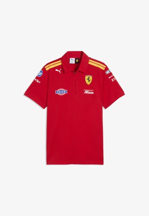 Czerwone polo z krótkim rękawem i żółtymi paskami na ramionach, logo Ferrari na piersi, logo Puma oraz kilka logo sponsorów na przodzie i rękawach.