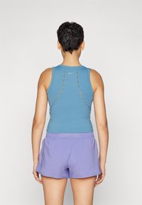 Sininen urheilullinen tank top, jossa on leikattu yksityiskohtia selässä, yhdistettynä purppuroihin shortseihin. Materiaali näyttää pehmeältä ja jouovalta.