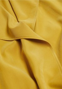 Tissu jaune drapé avec une texture lisse, présentant une légère brillance et des coutures nettes le long des bords, créant des plis doux et fluides.