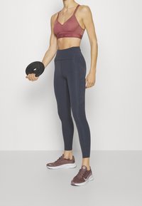 Conjunto deportivo que incluye un sujetador deportivo burdeos y leggings de tiro alto azul oscuro, con tejido texturizado y acentos reflectantes.
