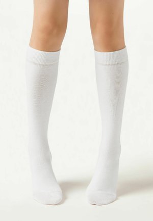Kniehohe weiße Socken aus weichem Stoff mit einem gerippten Bündchen. Sie verfügen über eine glatte Textur und eine nahtlose Zehenpartie für zusätzlichen Komfort.