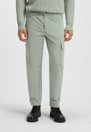 Lichtgroene cargobroek met twee zijzakken, gemaakt van soepele stof, met een comfortabele pasvorm en gestikte details. G gedragen met zwarte laarzen.