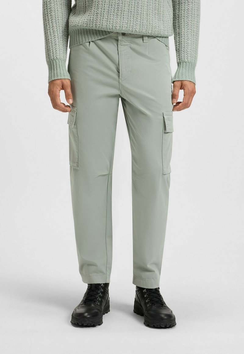 Lichtgroene cargobroek met twee zijzakken, gemaakt van soepele stof, met een comfortabele pasvorm en gestikte details. G gedragen met zwarte laarzen.