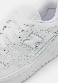 Bílé tenisky s perforovaným koženým svrškem, šněrováním a výrazným logem "N". Mají hladký povrch a gumovou podrážku s označením "new balance".