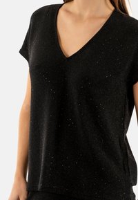 Top negro de cuello en v con mangas cortas, tejido texturizado con sutiles destellos, corte suelto y dobladillo recto.