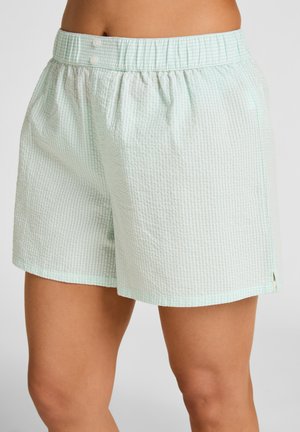 Shorts amples en seersucker vert clair avec taille élastique et deux boutons blancs, portés sur des jambes nues sur un fond neutre.