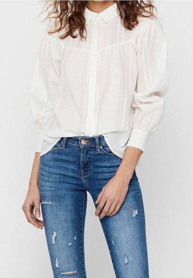 Vit, texturerad blus med krage och knappstängning, med vertikala ränder; kombinerad med slitna blå jeans.