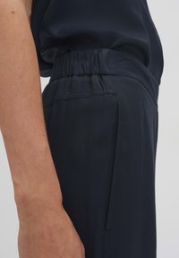 Marineblauwe broek met een relaxte pasvorm, voorzien van een elastische tailleband, zijzakken en een gladde stofstructuur.