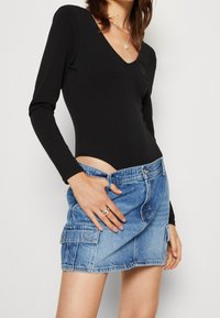 Svart långärmad bodysuit med V-ringning och skuren midja, tillsammans med en ljusblå denimminikjol med fickor och fransad nederkant.