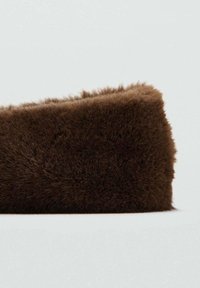 Producto de pelo sintético marrón con forma rectangular, que presenta una textura suave y esponjosa, con un borde ligeramente redondeado, colocado sobre un fondo neutro.