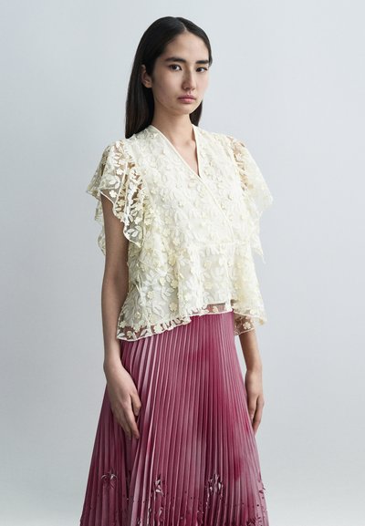 Top de encaje con bordado floral en color marfil, mangas con volantes en capas, combinado con una falda plisada degradada en tonos de rosa a burdeos.