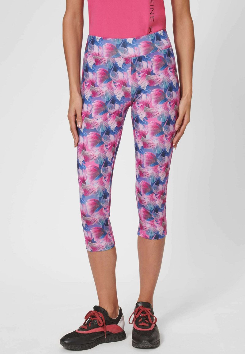 Bloemen capri leggings met een roze en blauwe print, gemaakt van lichte rekbare stof. Gecombineerd met zwarte sportschoenen.