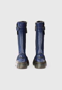 Μπότα από λουστρίνι υψηλή μέχρι το γόνατο σε ναυτικό μπλε χρώμα με γυαλιστερό φινίρισμα, μαύρο ύφασμα στην πλαϊνή πλευρά, κλείσιμο με φερμουάρ, ορατές κίτρινες ραφές και χοντρές σόλες.