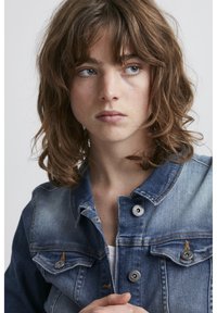 Giubbotto di jeans in tonalità di blu chiaro e medio, con colletto strutturato, tasche frontali e bottoni a pressione metallici con cuciture a contrasto.