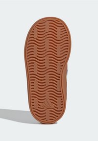 Gummisulor med ett vågigt mönster, i brun färg och texturerade greppsektioner. Adidas-logotypen syns på sulan.