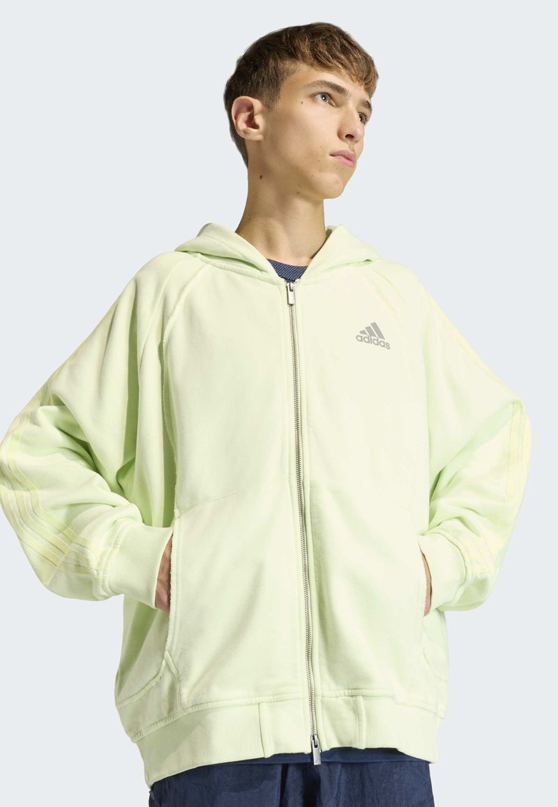 Sweat à capuche vert clair avec fermeture éclair, comprenant deux poches latérales et un design subtil à trois bandes sur les manches. Tissu en mélange de coton.