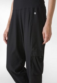 Zwarte geribde sportbroeken met een losse pasvorm, voorzien van een zijv pockets en een klein logo op de bovenste linkervoet.