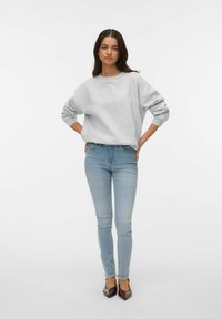 Pelēks džemperis ar plašām piedurknēm, kombinēts ar gaiši ziliem piegulošiem džinsiem un tumši brūnām kurpēm ar asu purngaliņu. Vienkāršs, ikdienišķs tērps.