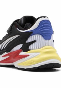 Baskets noires, blanches et rouges en mesh et matériaux synthétiques, avec une semelle extérieure incurvée jaune et des accents bleus près du talon.