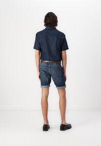 Chemise bleue marine à manches courtes avec des pois blancs, associée à un short en denim foncé retroussé et des chaussures noires. Une ceinture marron met en valeur la taille.