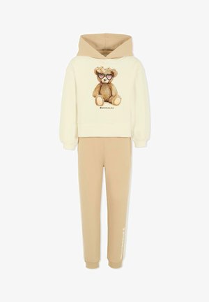 Beige katoenen hoodie en broek set. De hoodie heeft een teddybeer graphic met zonnebril en sprankels. Zacht materiaal met geribbelde boorden.