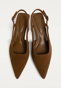 Tacchi slingback in suede marrone con punta affusolata, cinturino regolabile e lati aperti. Caratterizzati da una fodera interna liscia e un design minimalista.