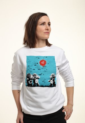 Felpa bianca con una grafica blu di orsetti su uno sfondo a muro testurizzato, con un cuore rosso sopra di loro. Collo rotondo semplice e maniche lunghe.