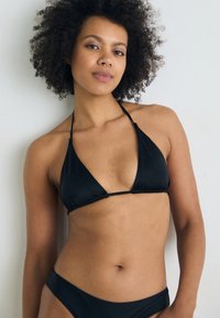 Čierny bikiny set s trojuholníkovým topom a tenkými ramienkami a zodpovedajúcim nízkym spodkom. Hladká textúra, minimalistický dizajn.