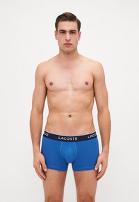 Boxer briefs de algodón azul con una cinturilla negra que presenta el logo de Lacoste. Diseño ajustado, textura suave y longitud hasta el muslo.
