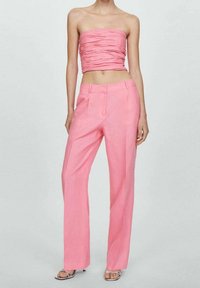 Top rosa sin tirantes con textura fruncida, combinado con pantalones rosa de pierna ancha y cintura alta. La modelo lleva sandalias con tacón transparente.