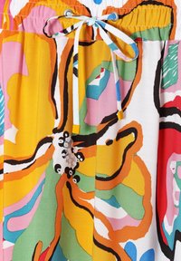 Pás s bílou šňůrkou uvázanou do mašle na barevném látce s odvážnými abstraktními květinovými vzory v žluté, oranžové, zelené, růžové a černé.