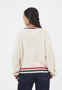 Maglione lavorato a maglia color crema con una vestibilità ampia, caratterizzato da accenti a strisce rosse e blu navy sul collo e sui polsini. Il retro mostra una texture a coste.