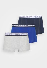 Three pairs of boxer shorts in grey, navy, and blue cotton. Each features a white band with "GANT" printed in navy. Smooth texture.