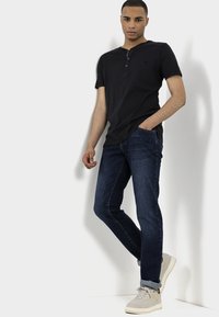 Black short-sleeve henley shirt with button accents, paired with dark blue jeans and light gray sneakers. Simple, casual outfit.