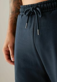 Pantalones deportivos de color navy con cinturilla ajustable mediante cordón, que presentan una textura suave y lisa, además de detalles metálicos en el cordón.